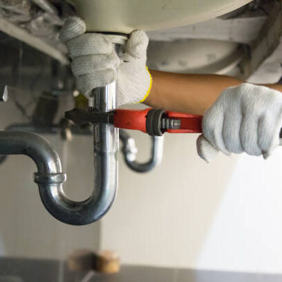 Plumber fixing white sink pipe with adjustable wrench.