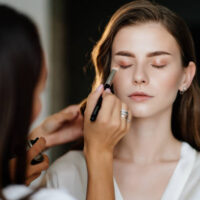 A beautiful young woman with long hair doing makeup for a wedding or photo shoot. the work of a make-up artist. the morning of the bride. decorative cosmetics.