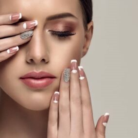 Young appealing woman is showing pale-pink french style manicure with  rhinestone on the slender fingers. Perfect makeup and trendy manicure.